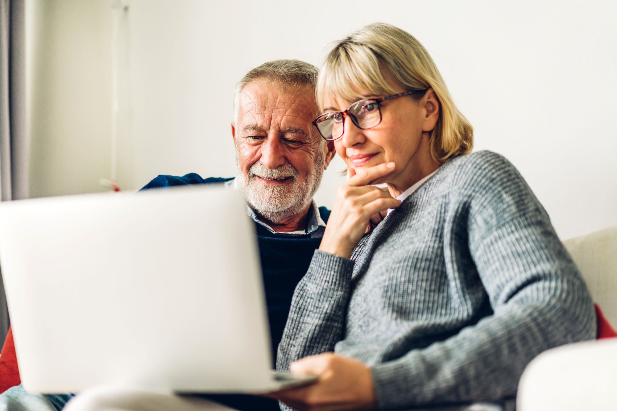 Senior couple looking at the laptop sitting on a sofa
